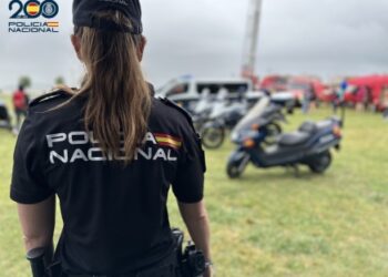 Agente de la Policía Nacional de espaldas durante un evento al aire libre, con motocicletas y vehículos de emergencias al fondo, conmemorando el bicentenario del cuerpo policial.