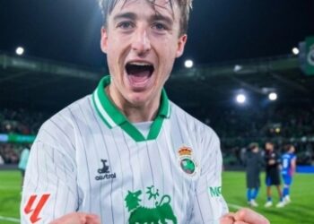 Jugador del Racing de Santander celebrando eufórico sobre el césped de los Campos de Sport de El Sardinero, tras un partido decisivo con ambiente vibrante en la grada.