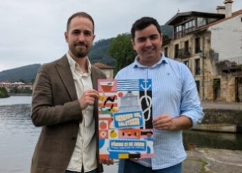 Presentación del cartel del Mercado del Solsticio en Limpias, con dos representantes municipales posando junto a la ría, anunciando la programación de food trucks, talleres y música para el sábado 21 de junio.