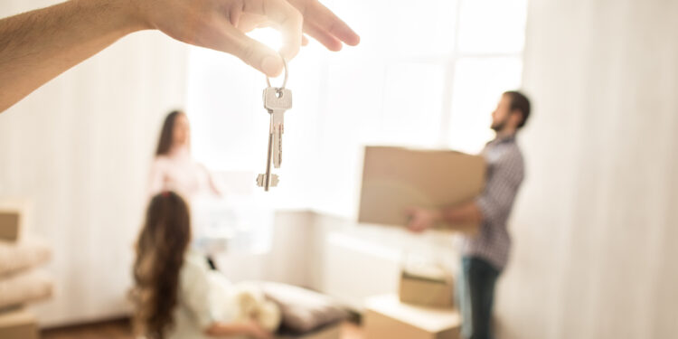 Nice picture of family working together. Man and woman are holding boxes while their child wants to help them. THere is a hand with set of keys in front of the picture